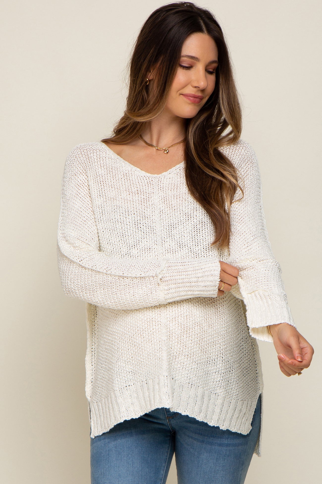 Woman wearing a cream oversized v-neck knit sweater and blue jeans against a neutral background