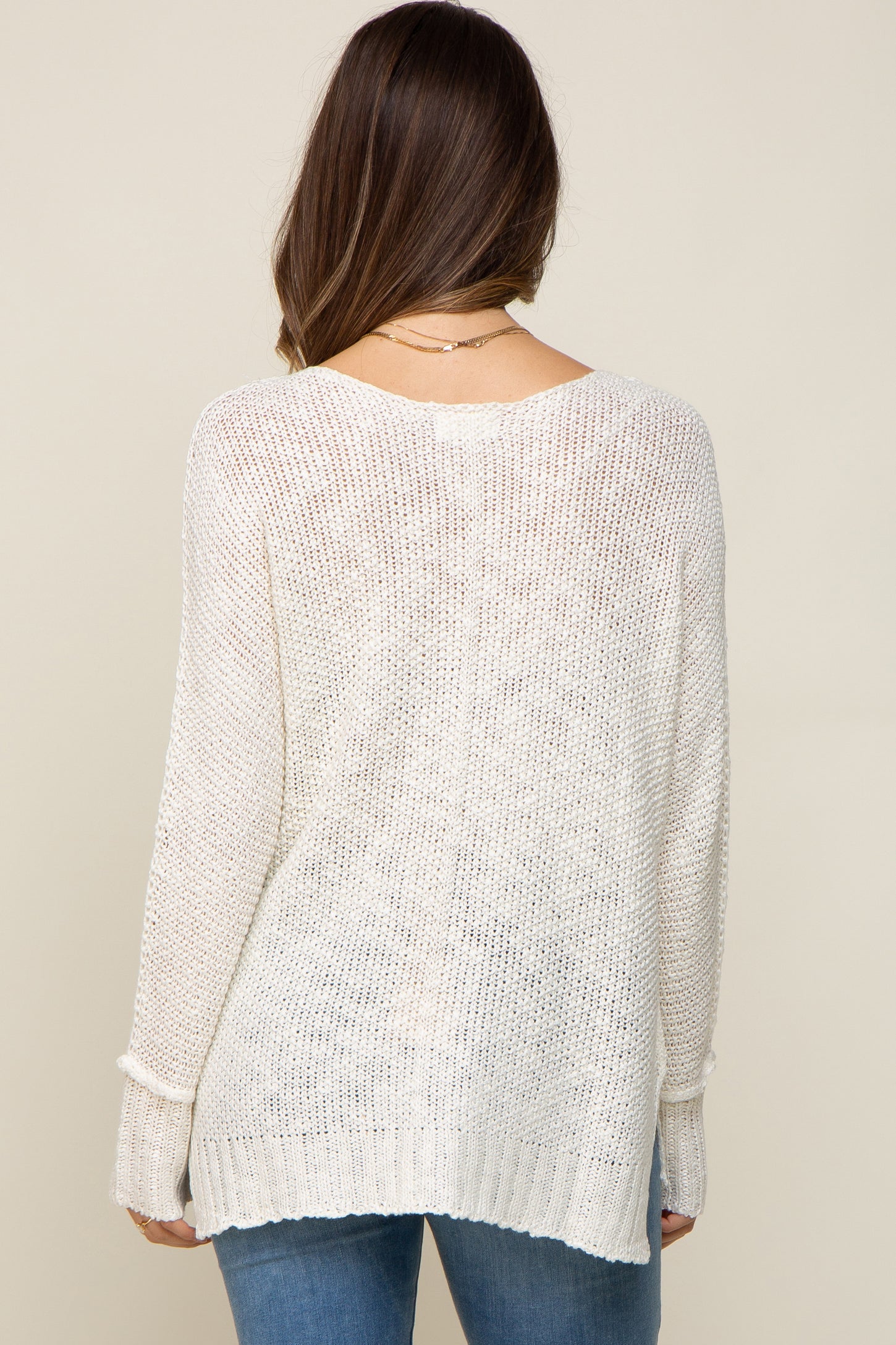 back view of a woman wearing a cream lightweight knit sweater and blue jeans
