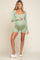 woman wearing a light green long sleeve maternity romper and holding her baby bump