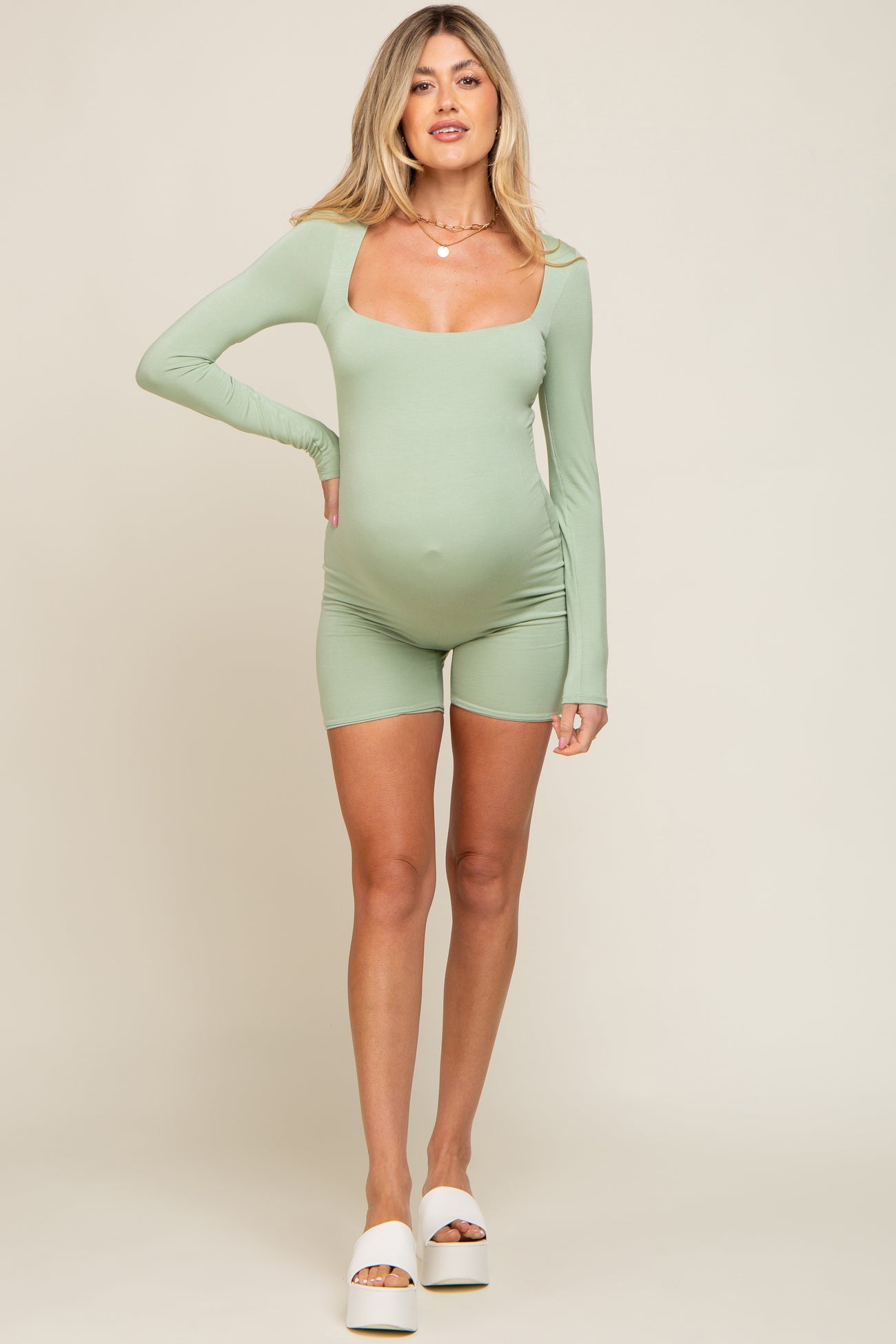 woman wearing a light green long sleeve maternity romper showcasing her baby bump