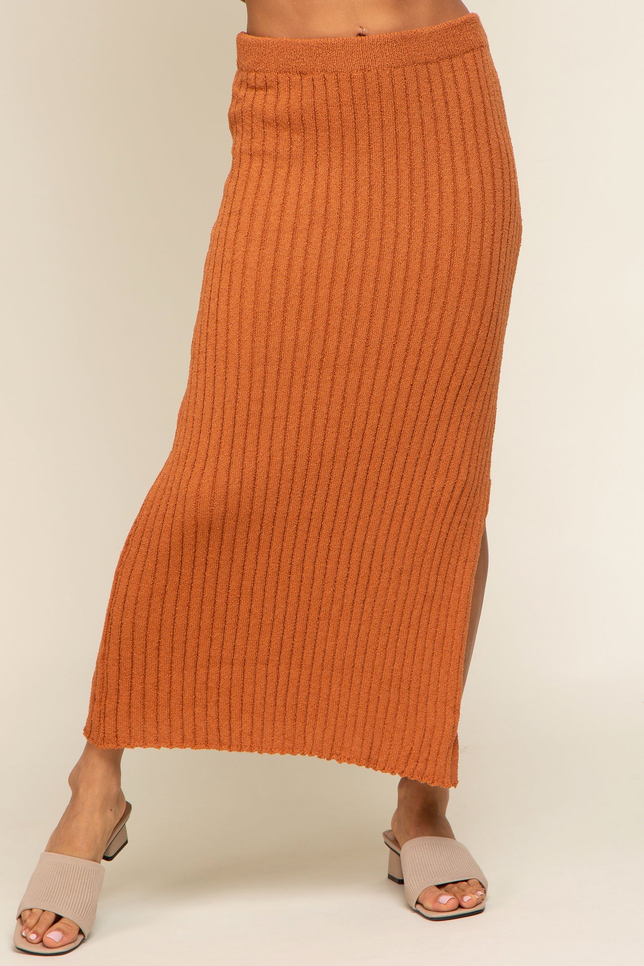 woman wearing a rust orange ribbed knit midi skirt with a side slit and beige slide sandals