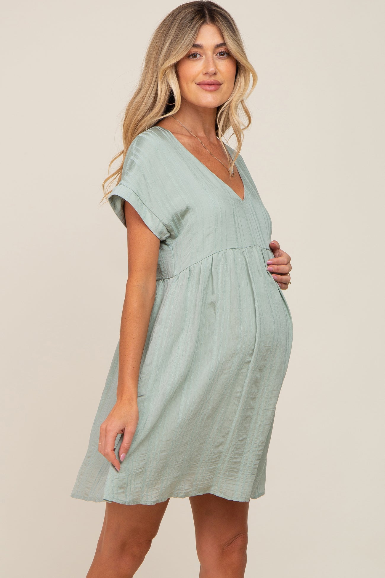 Pregnant woman wearing a light green v-neck maternity dress with short sleeves and textured fabric