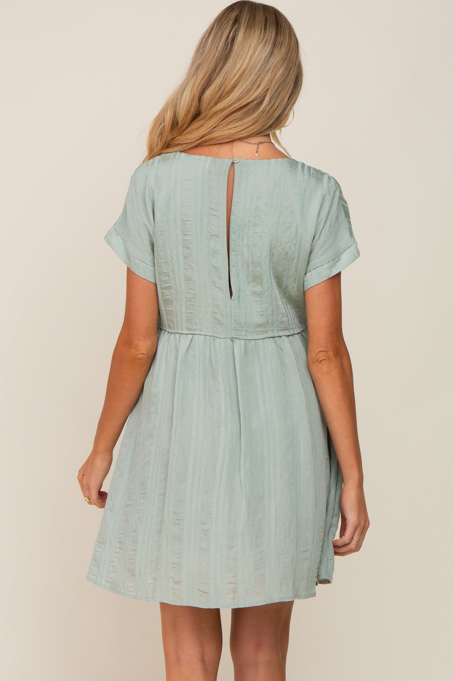 Back view of a woman wearing a sage green textured mini dress with short sleeves and a keyhole back detail