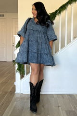 woman wearing a short denim dress with tiered ruffles and bell sleeves, paired with black cowboy boots