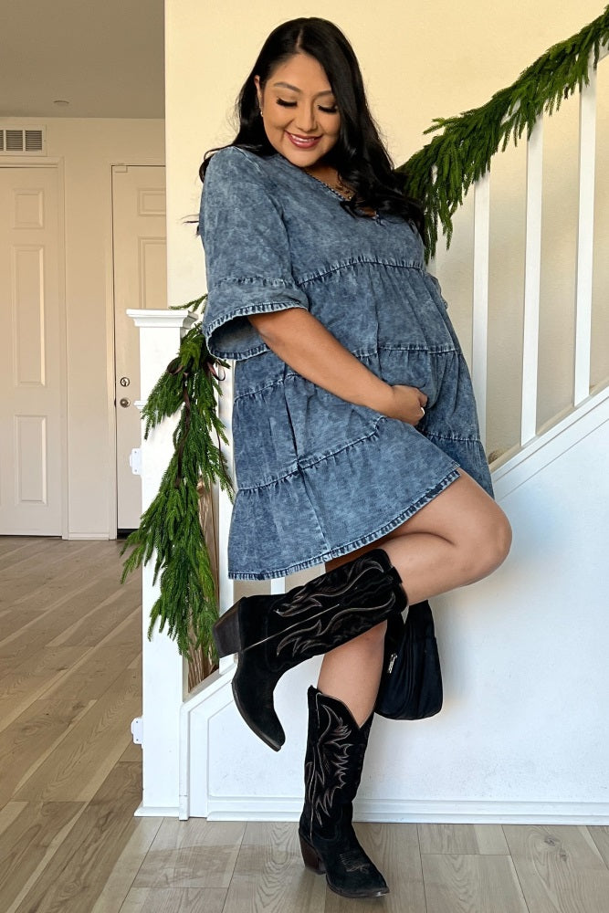 woman wearing a blue denim maternity dress with frayed edges, showing her baby bump, paired with black cowboy boots