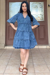 woman wearing a denim tiered maternity dress with short sleeves and a v-neckline, standing in front of a double door