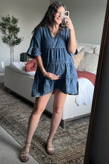 woman wearing a denim maternity dress with tiered ruffles, holding her baby bump in a mirror selfie