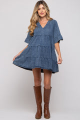 woman wearing a denim tiered maternity dress with a v-neck and flared sleeves, paired with brown knee-high boots