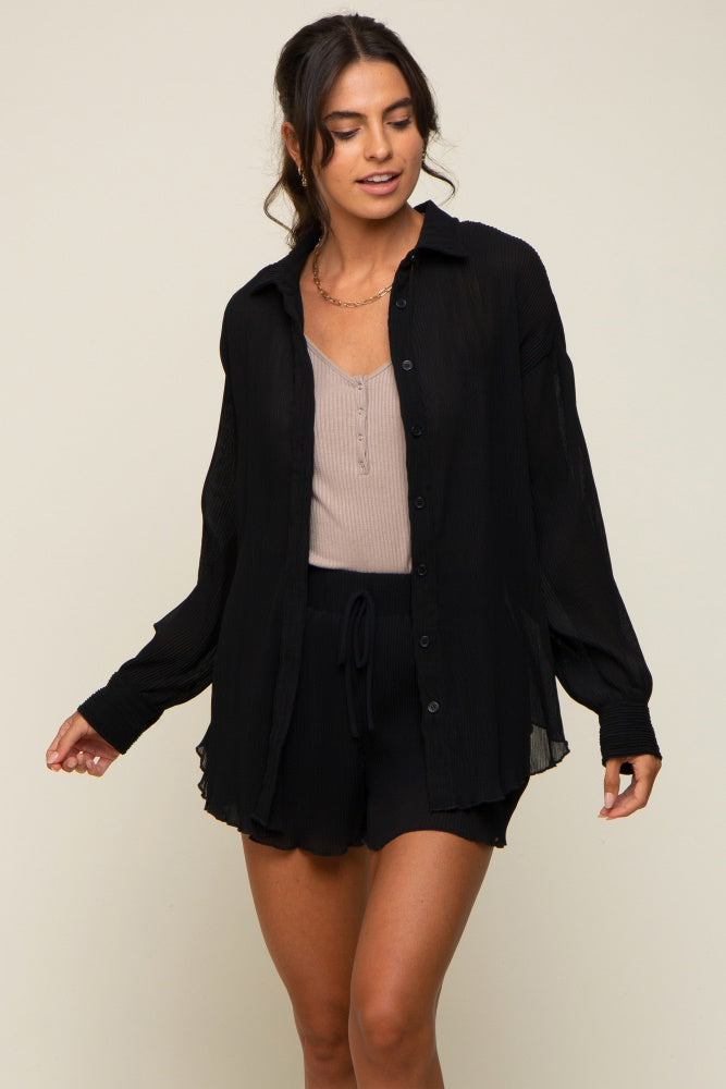 woman wearing a black long sleeve button down shirt over a tan top and matching black drawstring shorts