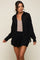 woman wearing a black long sleeve button down shirt over a tan top and matching black drawstring shorts