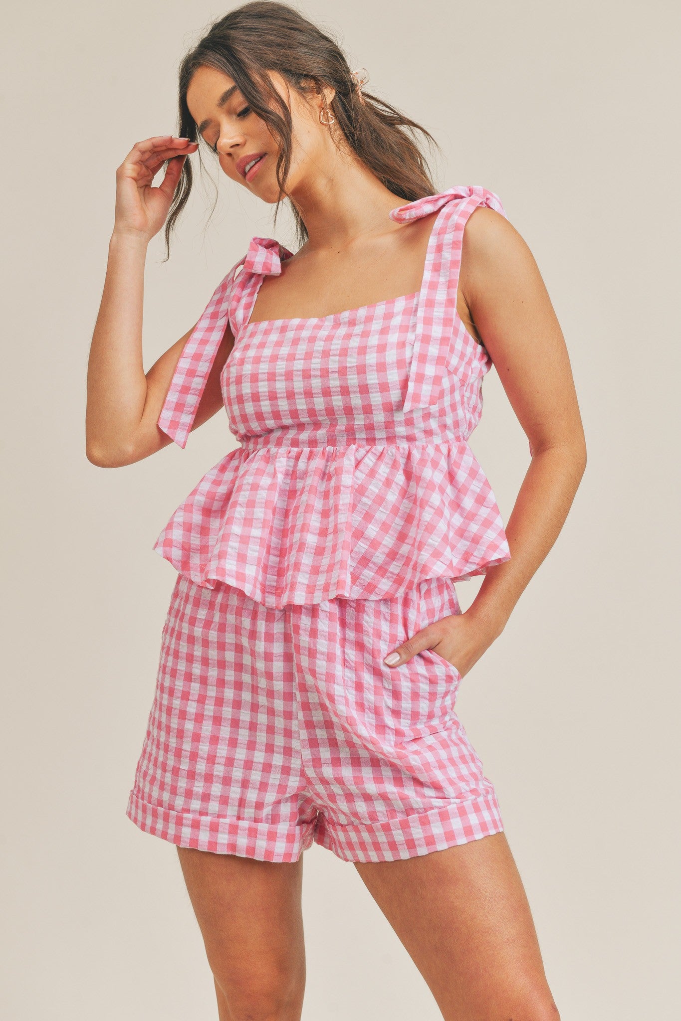 woman wearing pink and white gingham two-piece set with tie-shoulder peplum top and matching shorts