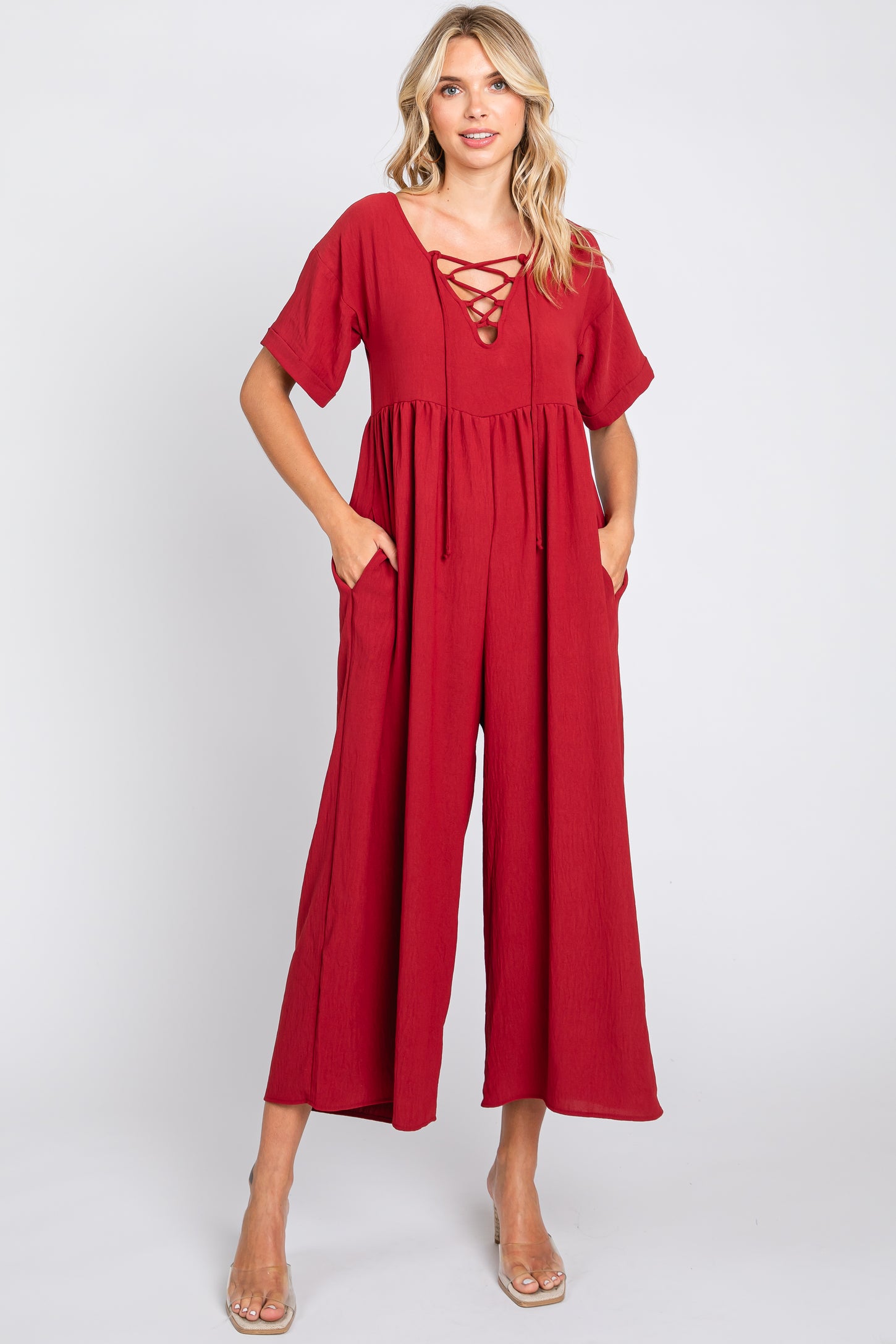 woman wearing a red short sleeve wide leg jumpsuit with lace up neckline and pockets