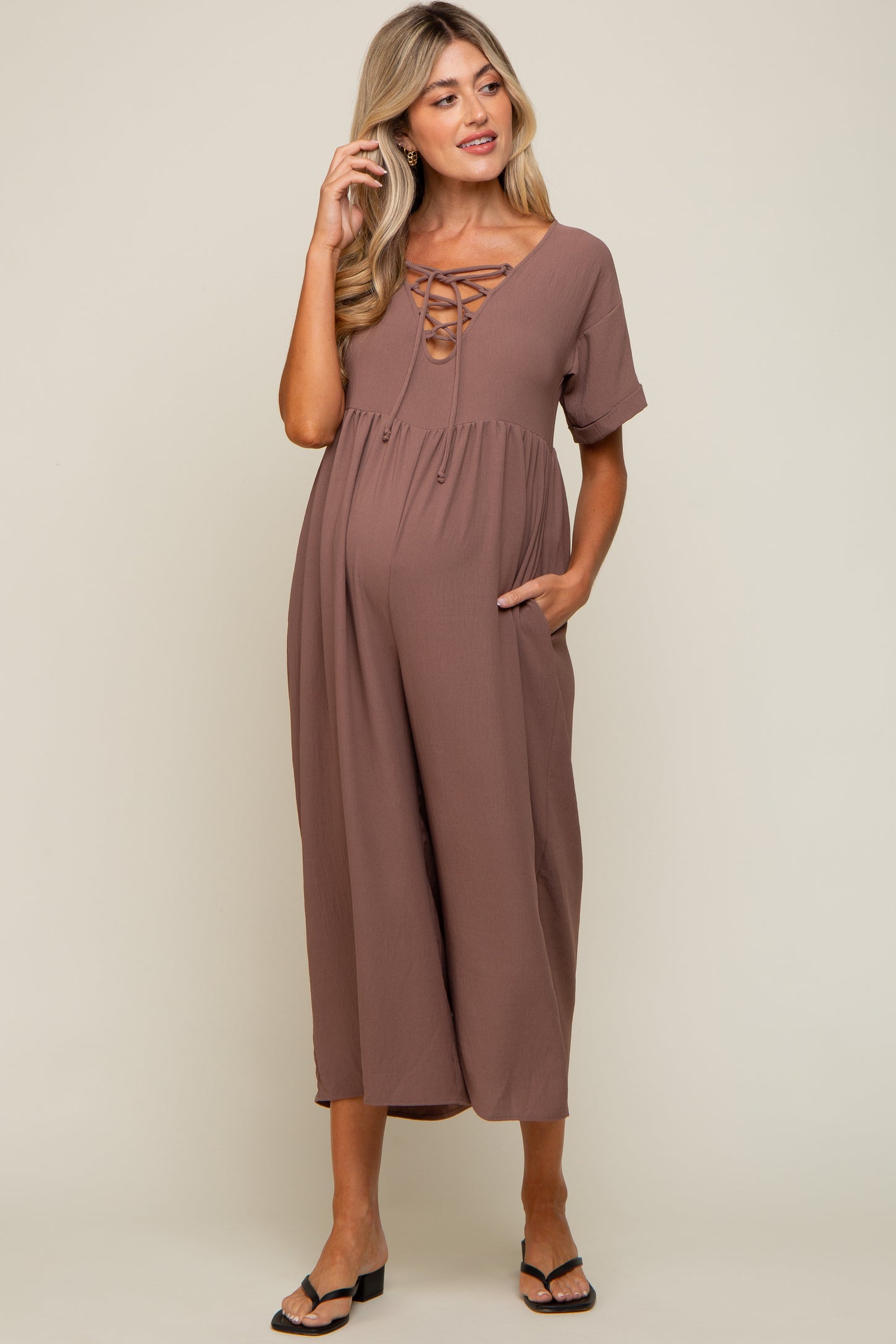 Pregnant woman wearing a mauve lace-up maternity jumpsuit with short sleeves and pockets