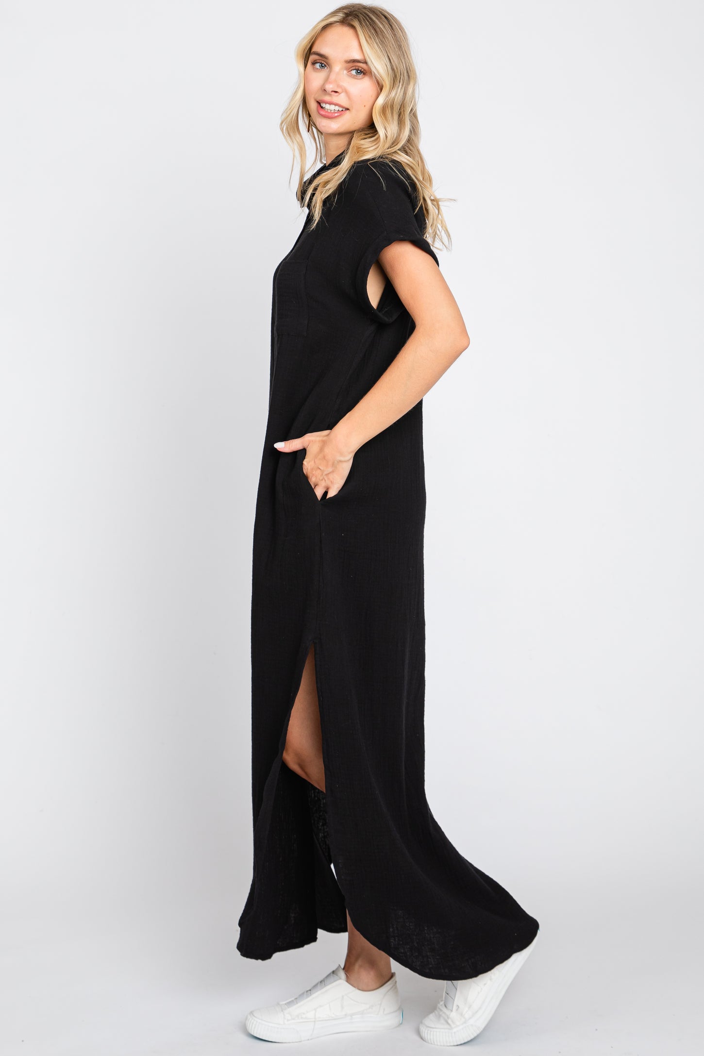 woman wearing a black sleeveless maxi dress with side slits and pockets, styled with white sneakers