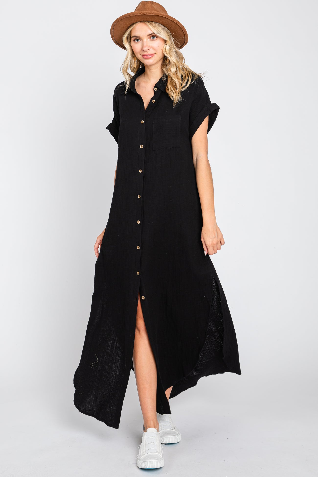 woman wearing a short sleeve black maxi dress with buttons and side slits, paired with a tan hat and white sneakers