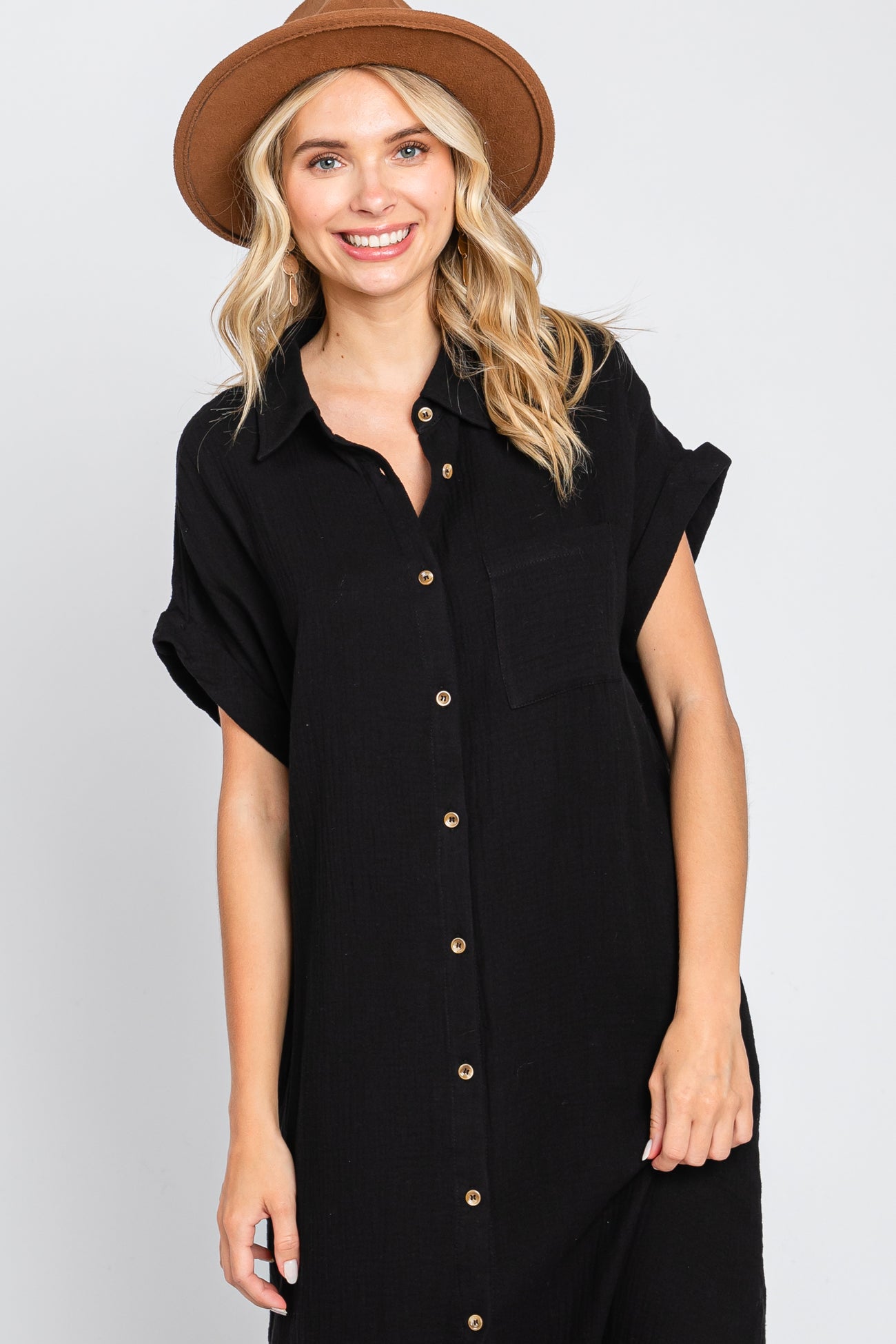 woman wearing a black button-up dress with short sleeves and a chest pocket, smiling and wearing a brown hat