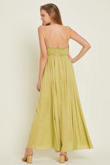 woman wearing a light green backless maxi dress with spaghetti straps and a smocked bodice, standing with her back to the camera