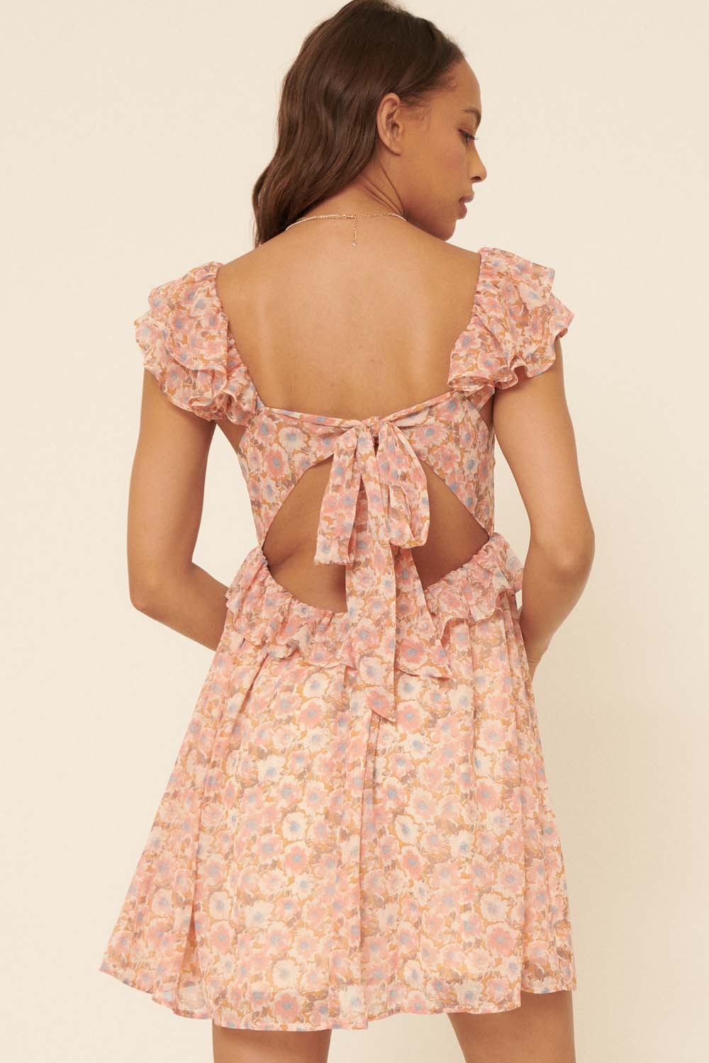 woman wearing a pink floral dress with ruffle sleeves and an open back featuring a tie detail