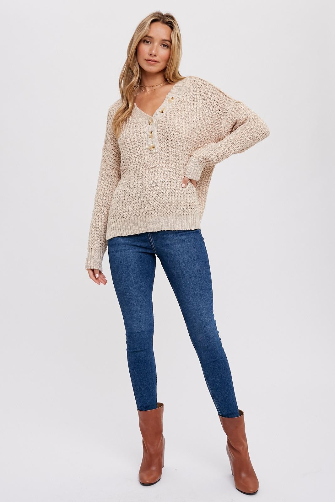 woman wearing a beige chunky knit sweater with button details and blue skinny jeans, paired with brown ankle boots