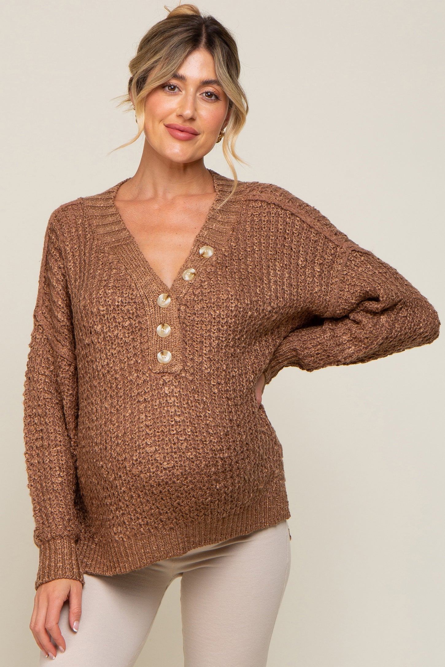 Pregnant woman wearing a brown textured knit maternity sweater with button-down v-neck and cream pants