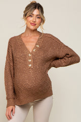 Pregnant woman wearing a brown textured knit maternity sweater with button-down v-neck and cream pants