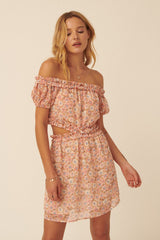 woman wearing a pink floral off-the-shoulder crop top and matching mini skirt with ruffle details