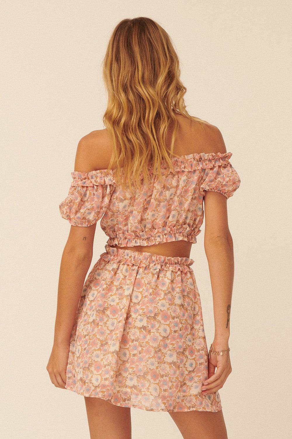 woman wearing a pink floral off-the-shoulder crop top and matching skirt, showcasing a ruffled design and back view