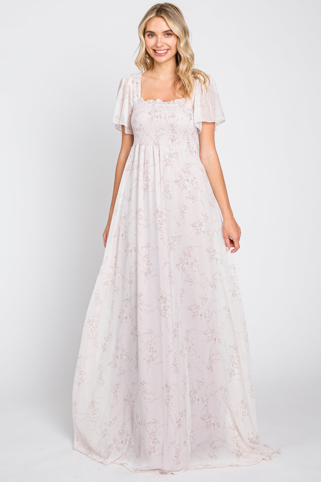 Woman wearing a light pink floral maxi dress with smocked bodice and flutter sleeves