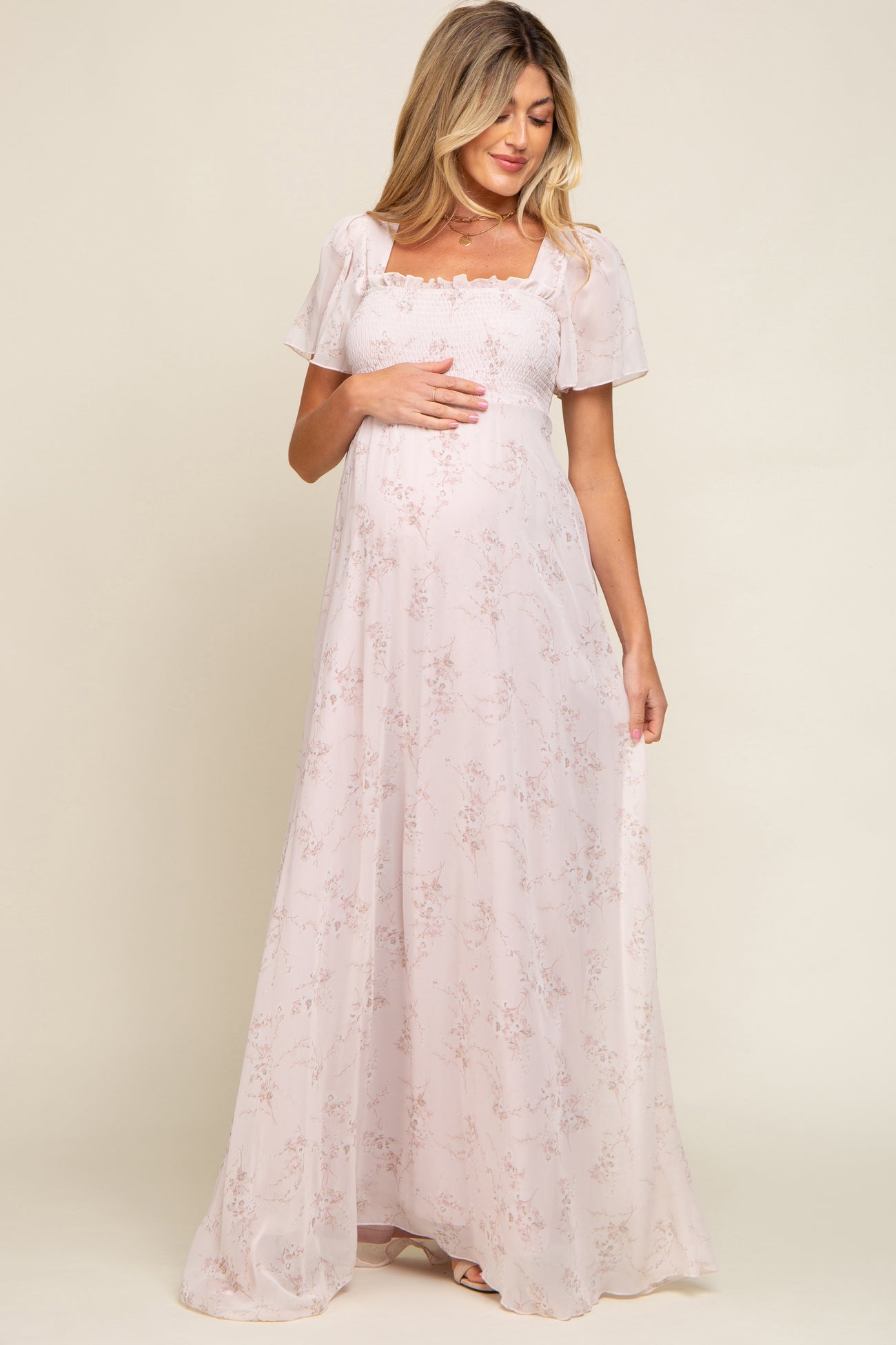 pregnant woman in light pink floral maternity maxi dress with smocked bodice and flutter sleeves