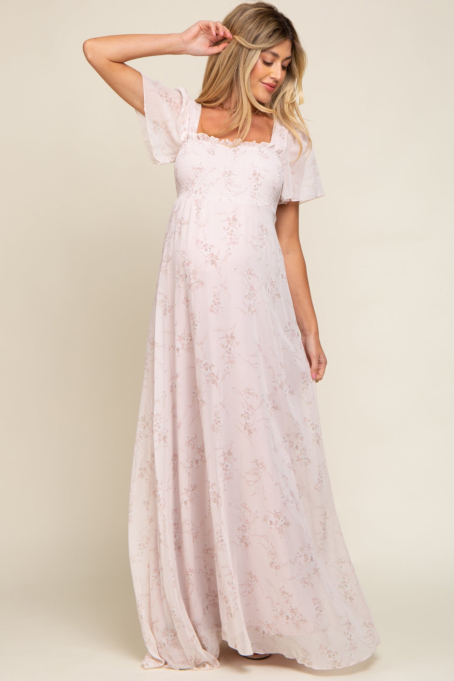 pregnant woman wearing light pink floral maternity maxi dress with smocked bodice and flutter sleeves