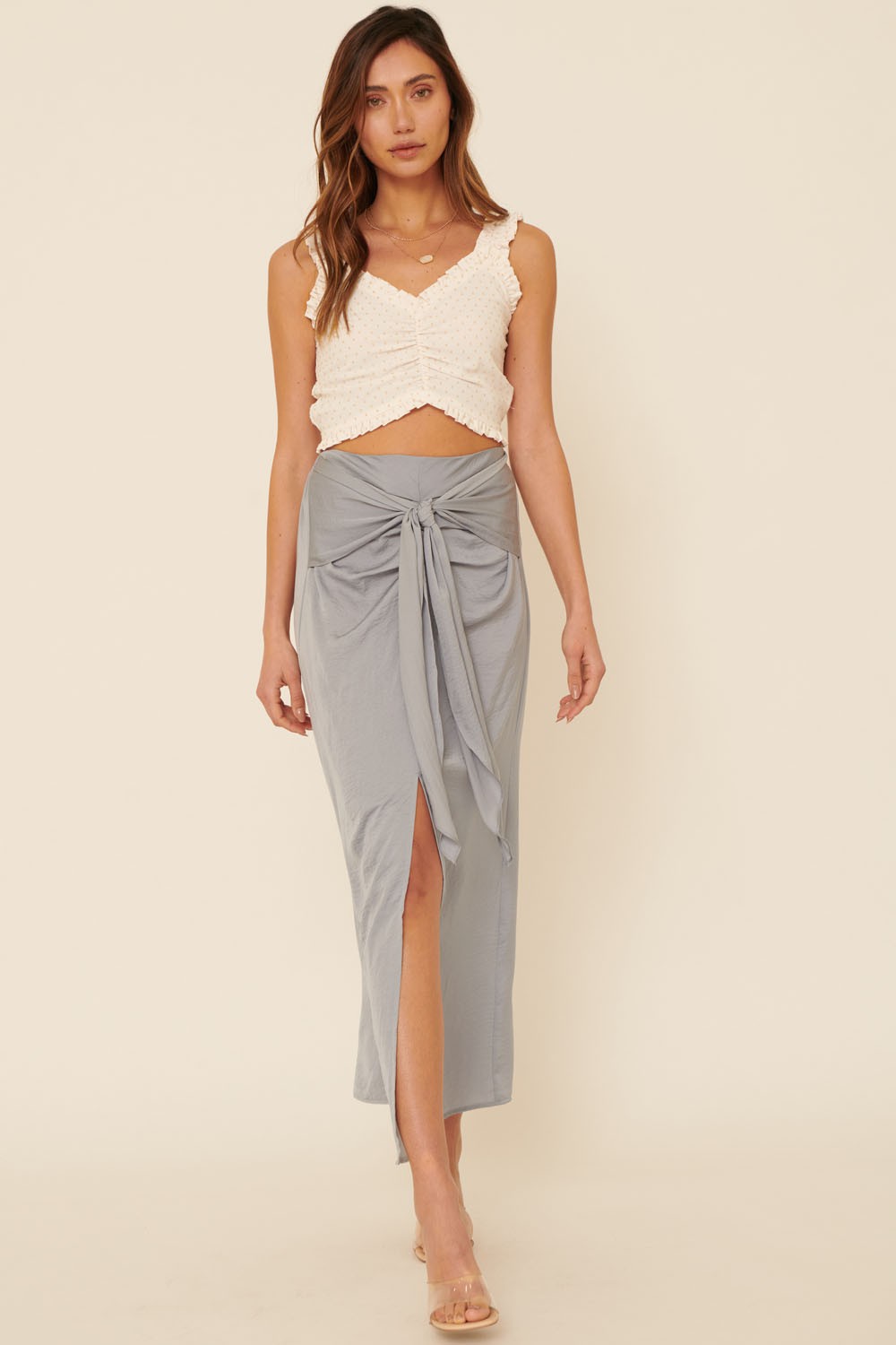 woman wearing a white ruffle crop top and a light gray tie-front maxi skirt with a side slit