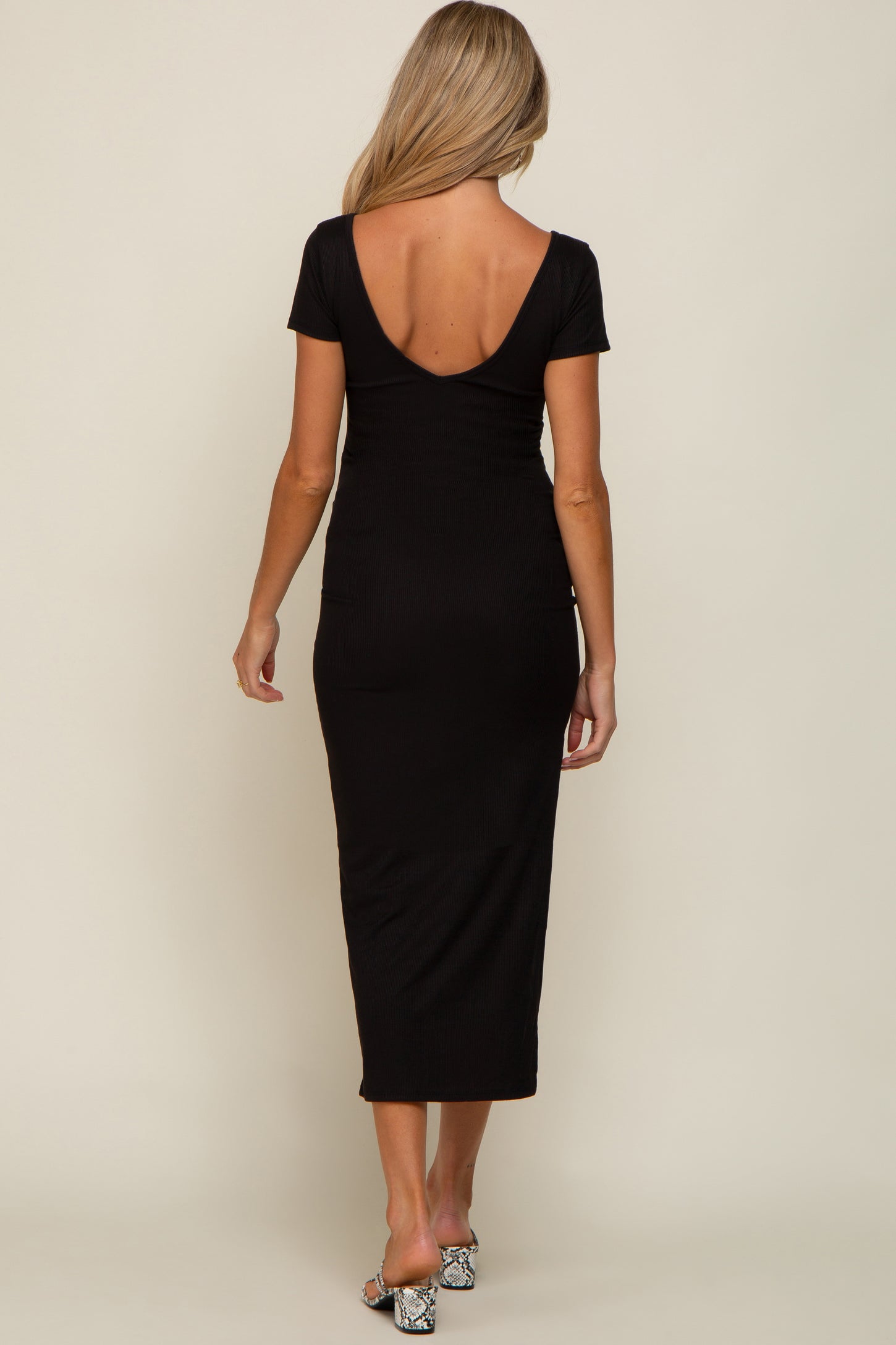 back view of a woman wearing a black short sleeve midi dress with a scoop back and snakeskin heels