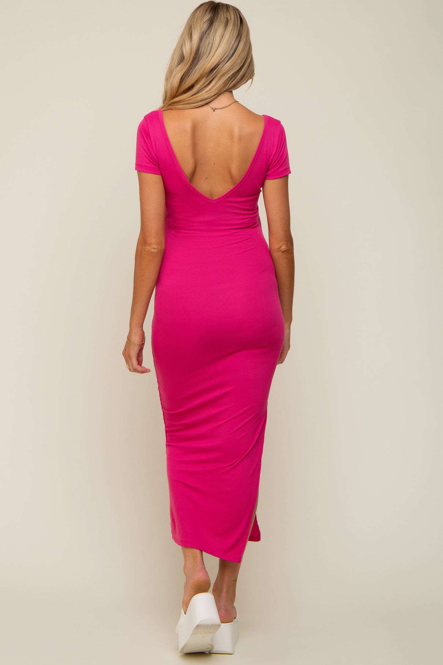 woman wearing a pink maternity dress with a deep V-back and short sleeves, showcasing a baby bump