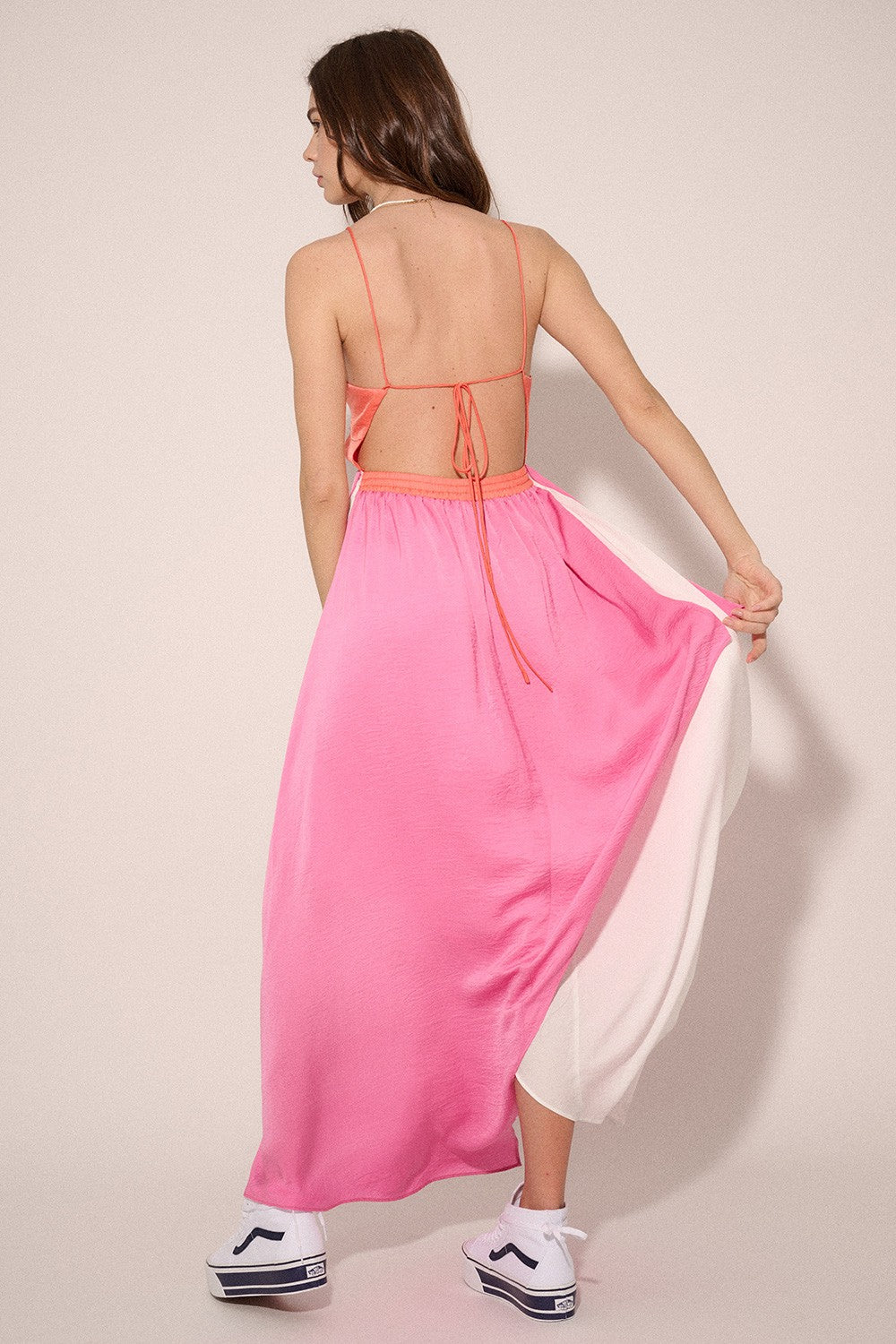 woman wearing a pink and white backless maxi dress with spaghetti straps and tied detail, paired with sneakers