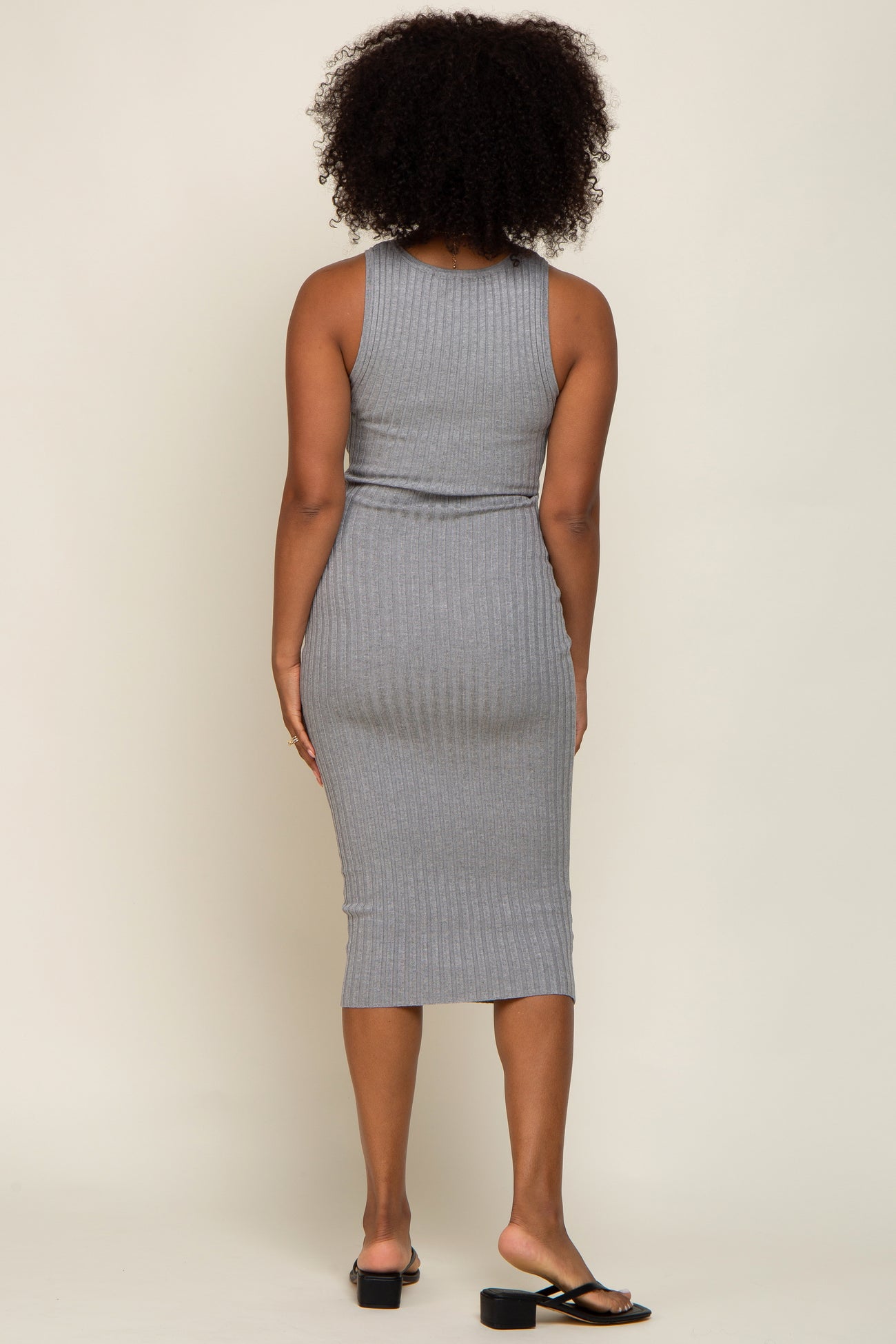 Back view of a woman with curly hair wearing a grey ribbed knit midi dress and black sandals