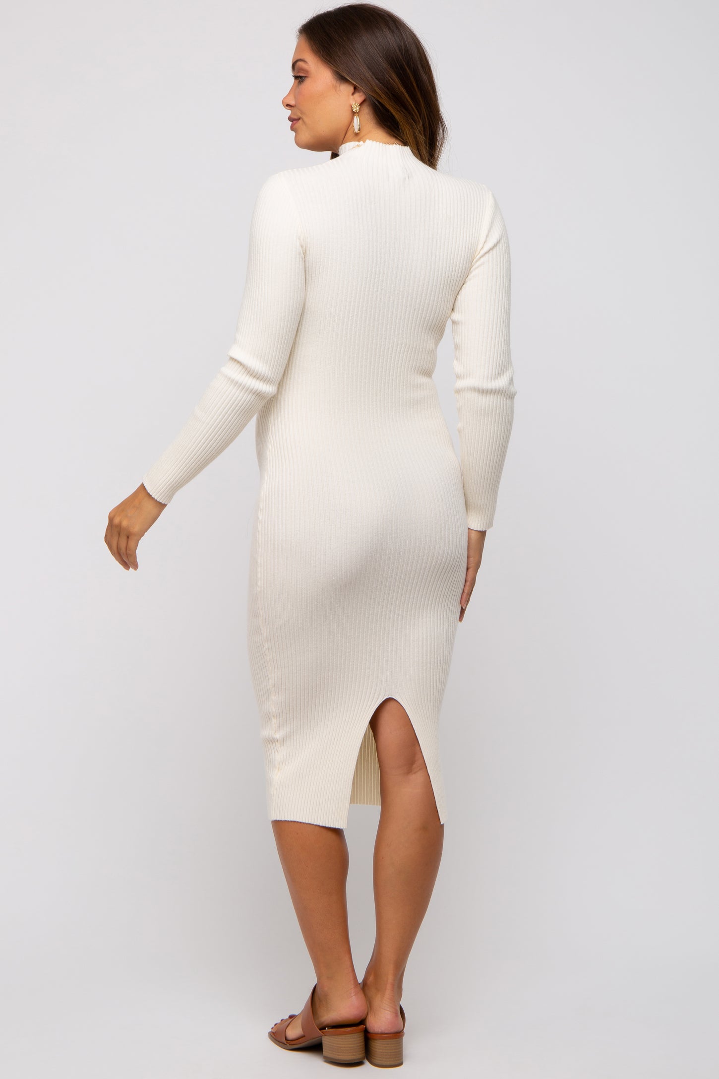 woman wearing a cream ribbed maternity dress with a back slit, showcasing her silhouette