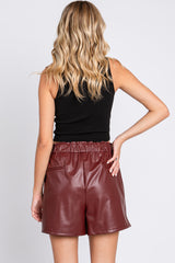 woman wearing a black tank top and burgundy faux leather shorts, showing the back view with elastic waistband