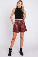 woman wearing a black sleeveless cropped top and burgundy faux leather shorts with an elastic waistband
