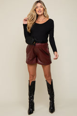 woman wearing a black long sleeve maternity top and burgundy faux leather shorts, paired with black knee-high boots