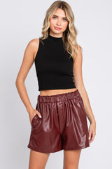 woman wearing a black sleeveless crop top and burgundy faux leather high-waisted shorts with pockets