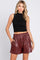 woman wearing a black sleeveless crop top and burgundy faux leather high-waisted shorts with pockets