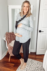 woman wearing a grey long sleeve maternity top and black jogger pants, gently cradling her baby bump