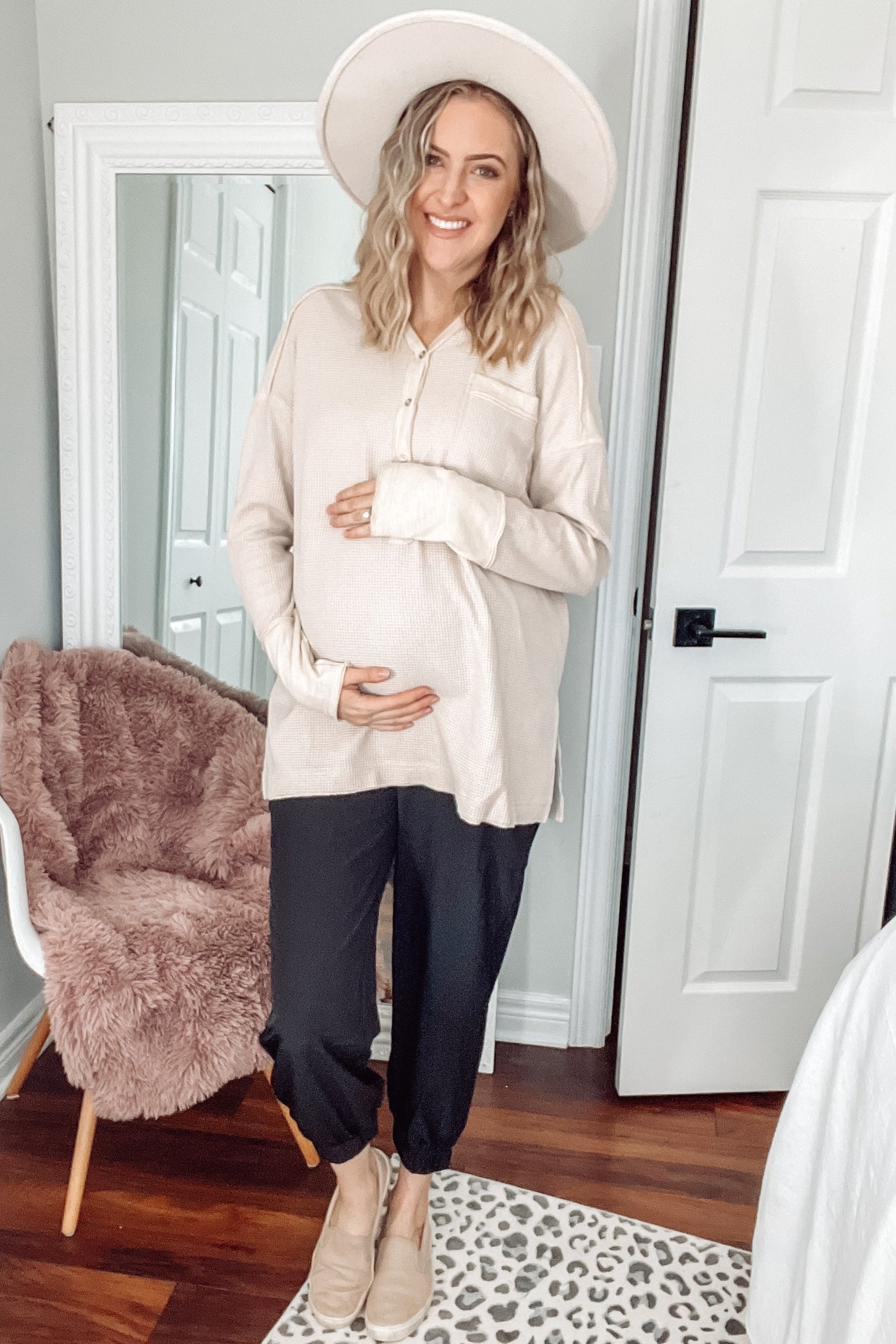 pregnant woman in cream waffle knit top and black joggers wearing a wide brim hat