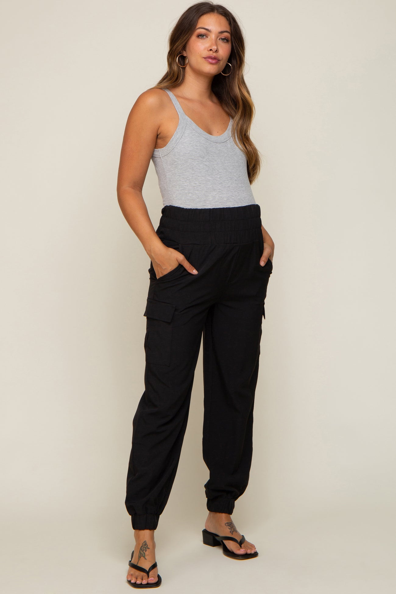 woman wearing a gray tank top and black maternity cargo pants with pockets and elastic cuffs, showcasing her baby bump