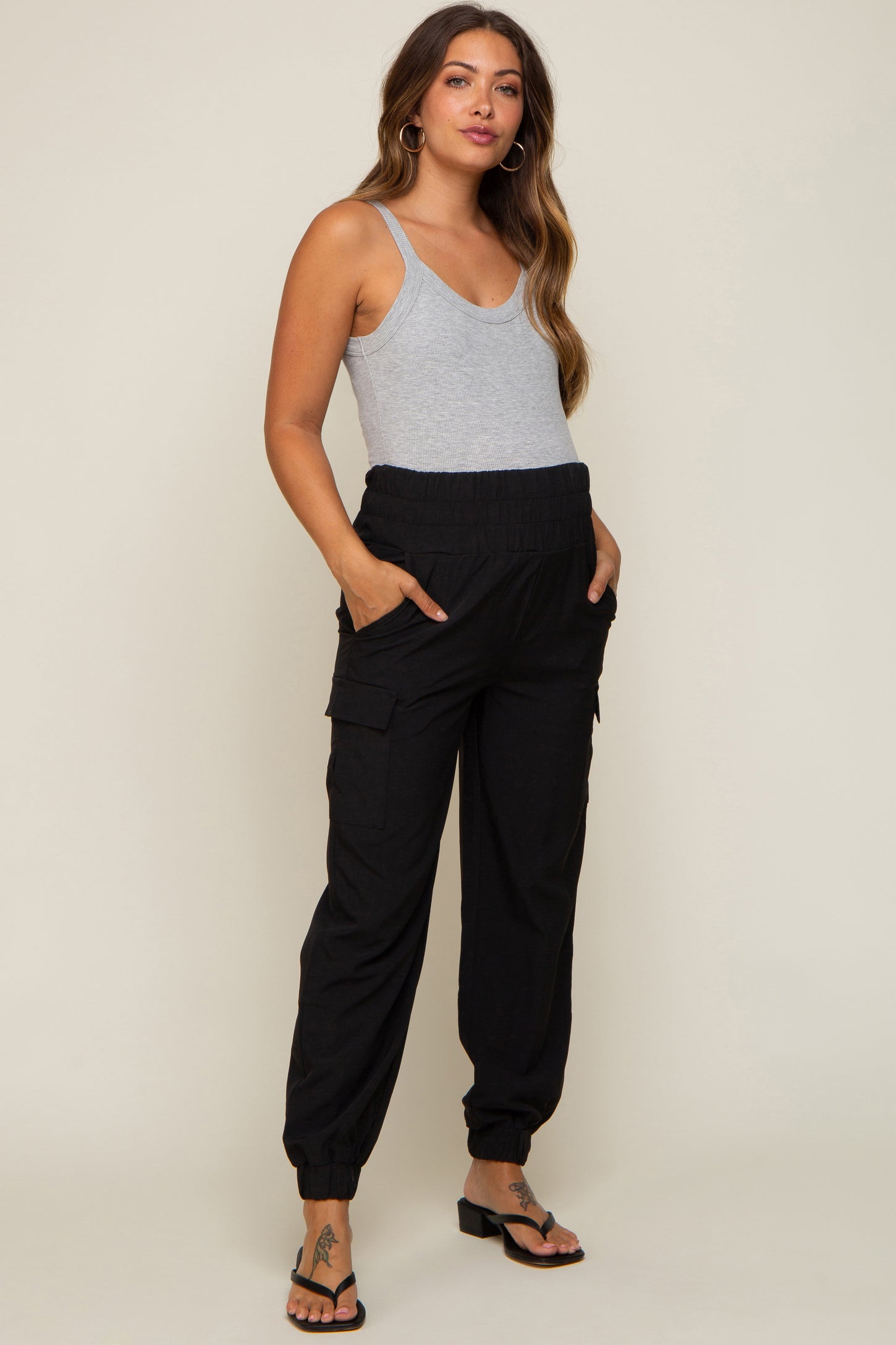 woman wearing a gray tank top and black maternity cargo pants with pockets and elastic cuffs, showcasing her baby bump