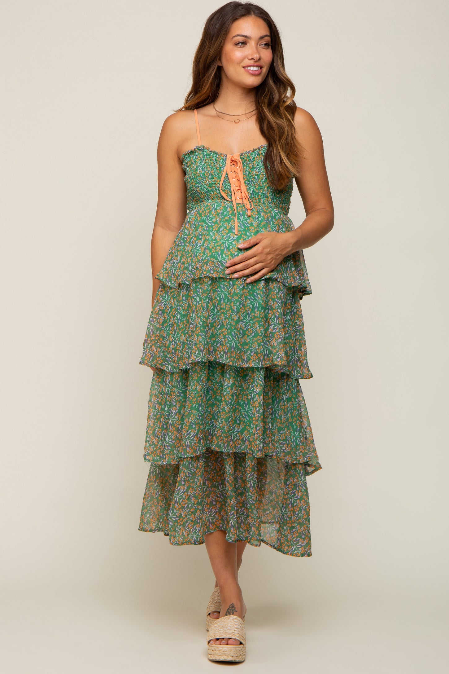 Pregnant woman in green floral tiered maternity midi dress with lace-up bodice and smocked detailing