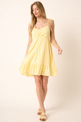 woman wearing a yellow short sundress with ruched detail and ruffled hem, styled with yellow sandals