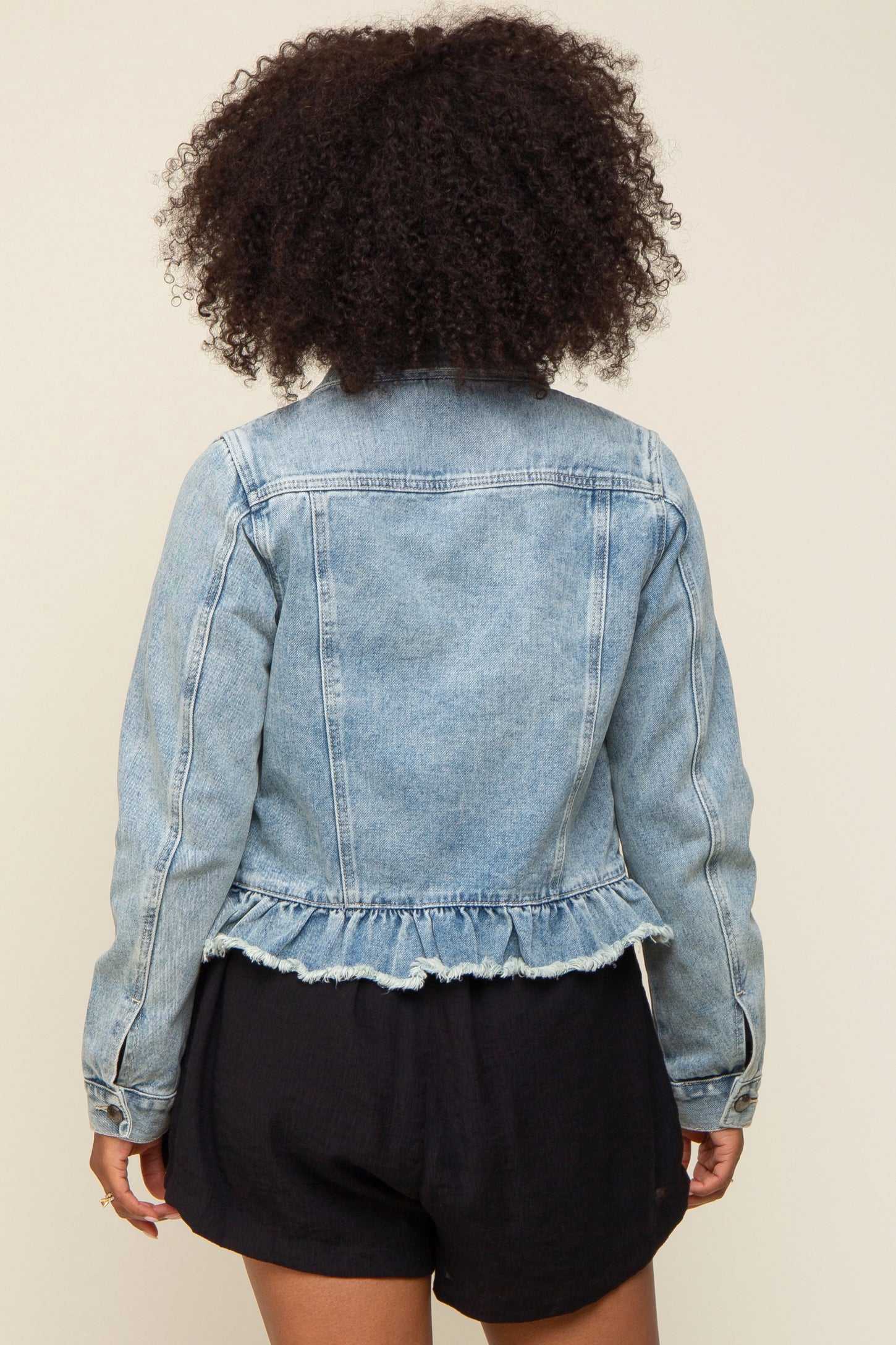 woman wearing a light blue denim jacket with a ruffled hem and long sleeves, viewed from the back