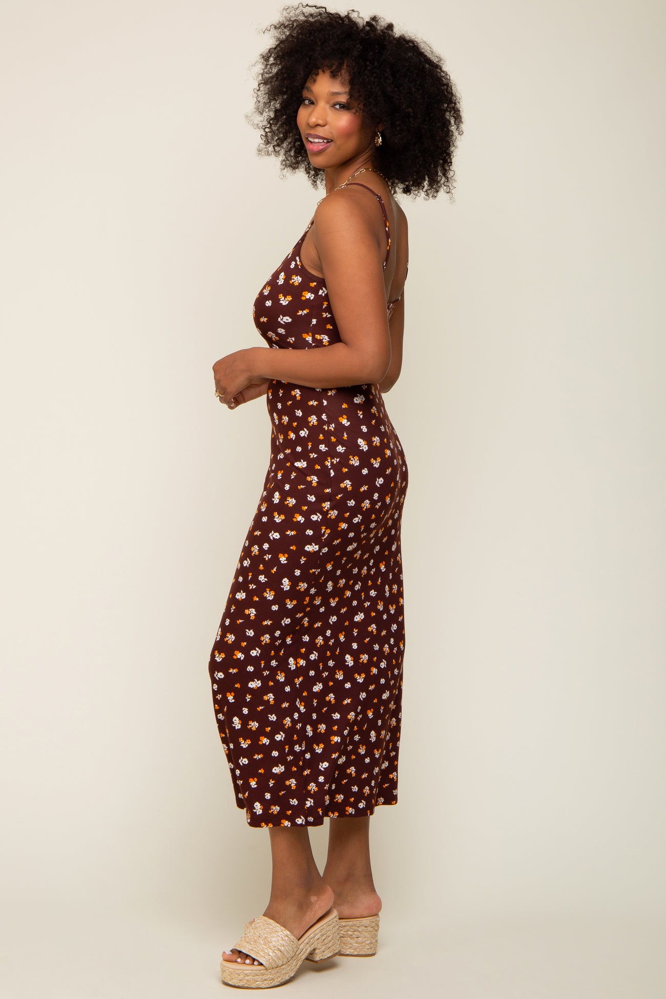 Woman with curly hair wearing a brown floral midi dress and platform sandals against a neutral background
