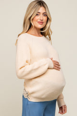 Pregnant woman in cream knit maternity sweater with lace trim holding her baby bump